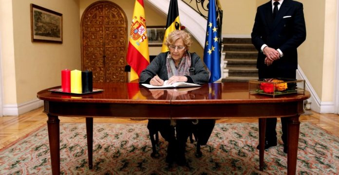 La alcaldesa de Madrid, Manuela Carmena (i), firma en el libro de condolencias que se ha abierto en la residencia del embajador de Bélgica, Pierre Labouverie (d), con motivo de los atentados cometidos ayer en Bruselas.